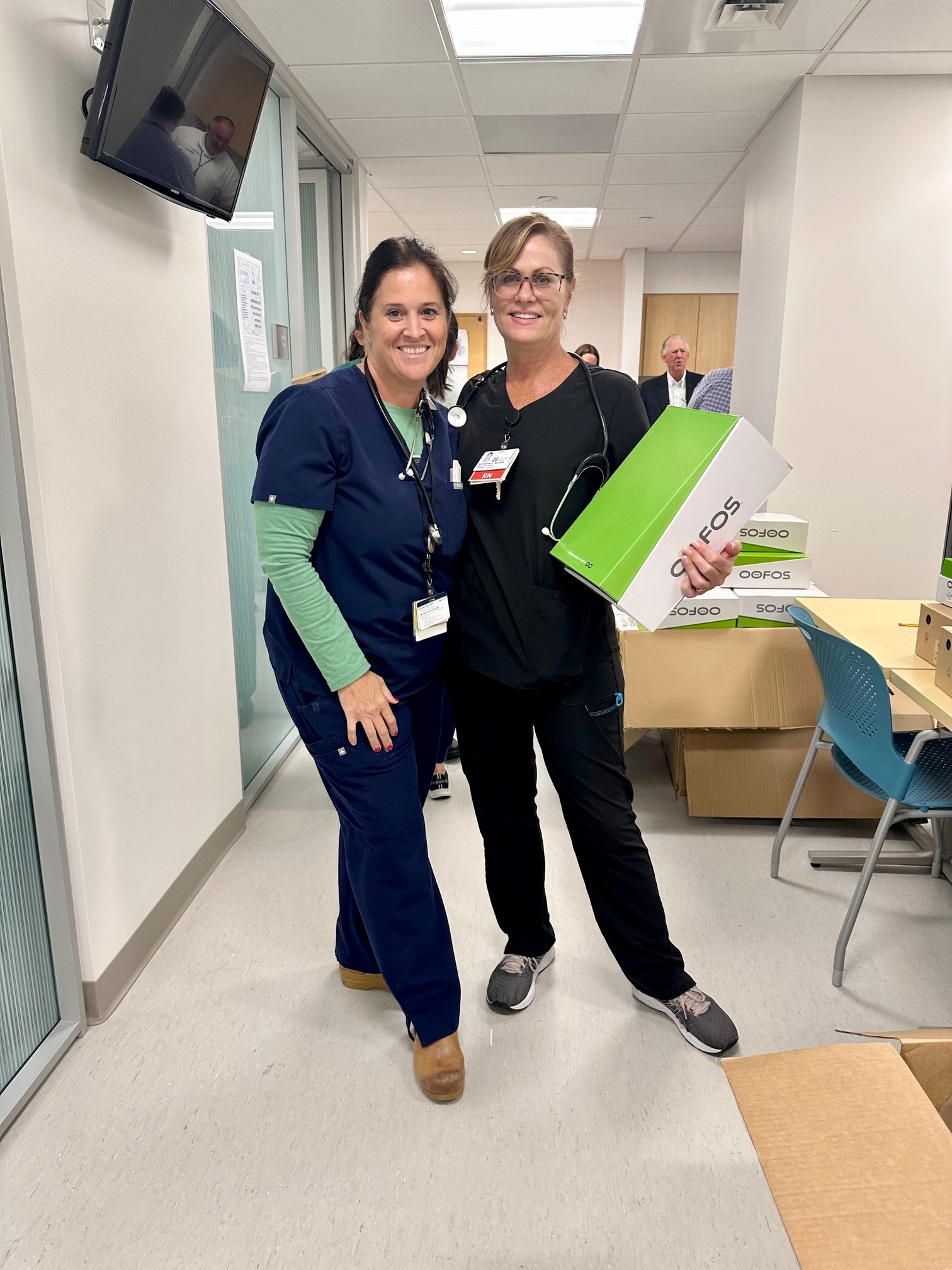 Two ED colleagues from South Shore Hospital, one holding a shoebox, pose for a photo after Oofos donated shoes to every ED colleague.