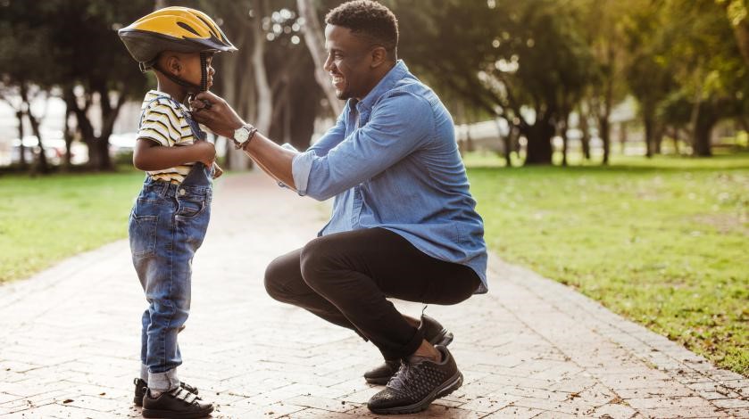 A dad adjusts the strap on his son's bike helmet