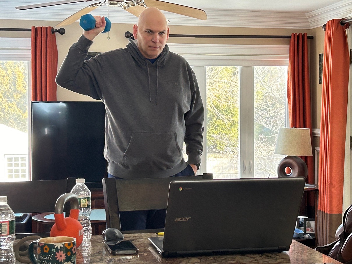 A man lifts a weight as he follows along with a virtual exercise class