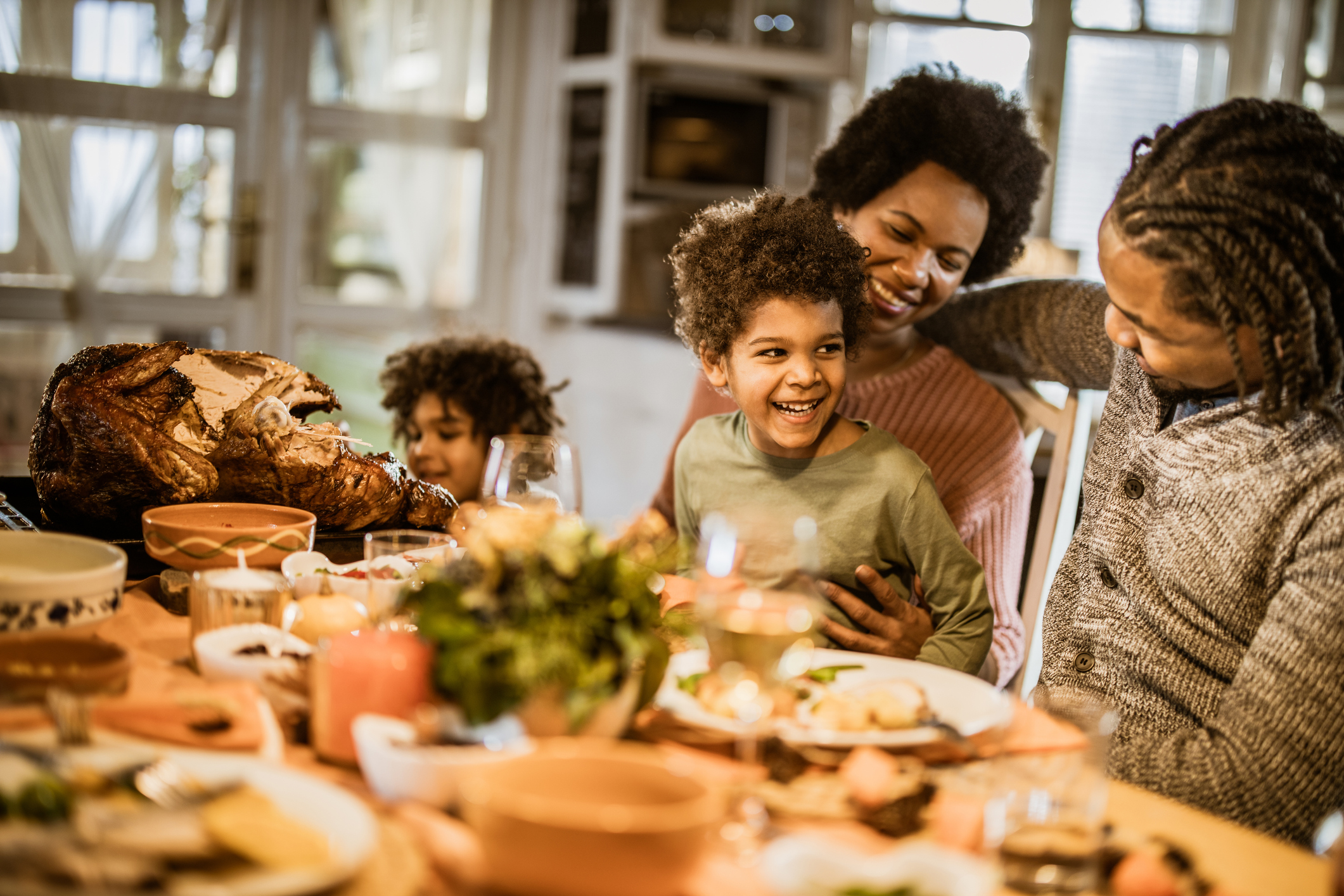A family of four, featuring two children, sits around a Thanksgiving dinner laid out on a table, smiling.