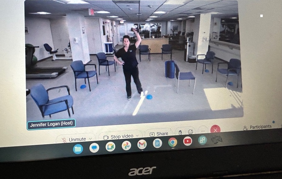 An female instructor leads a virtual exercise class seen on a laptop