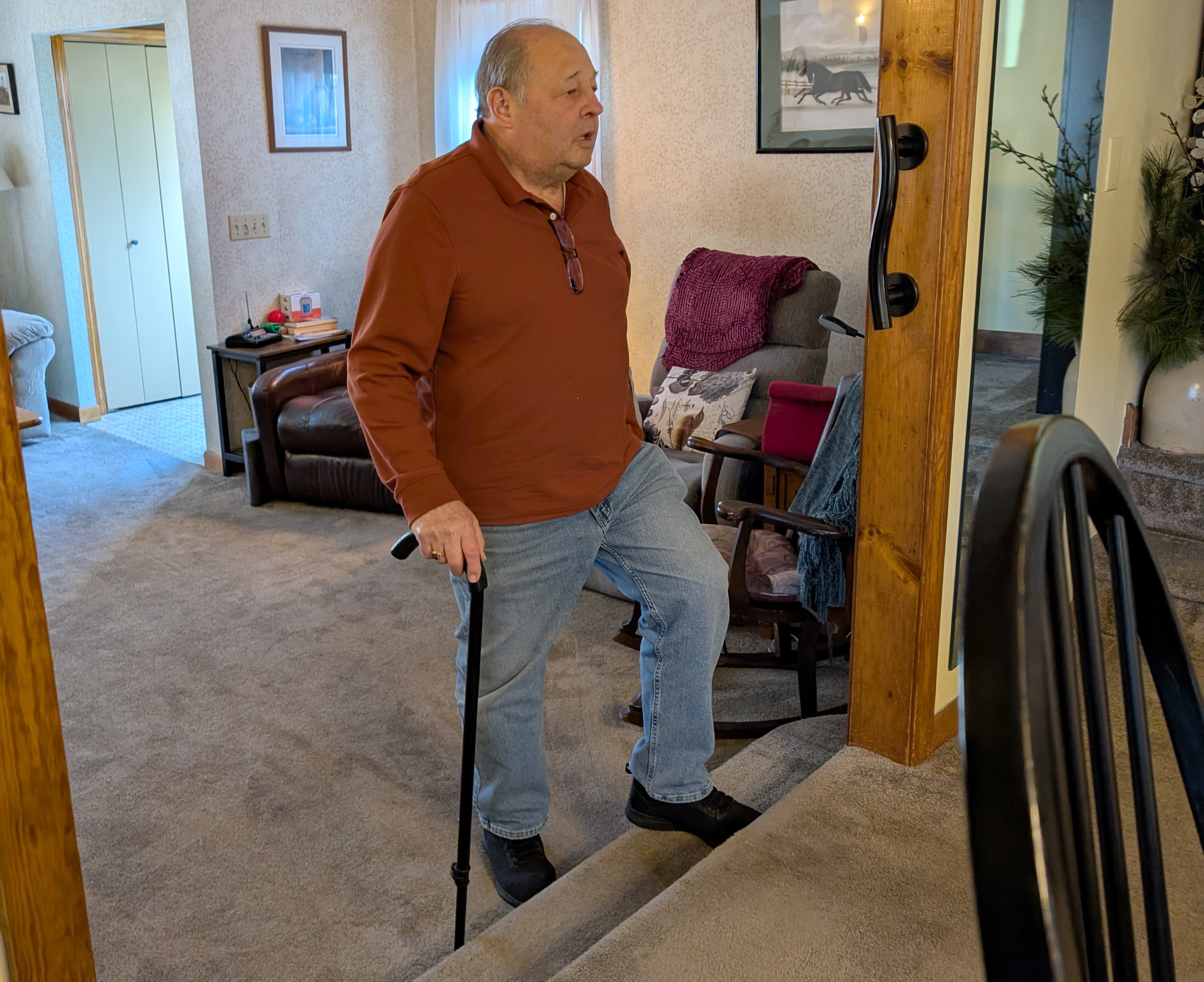 John of Rockland uses his cane to climb up steps at his house during an at-home physical therapy appointment.