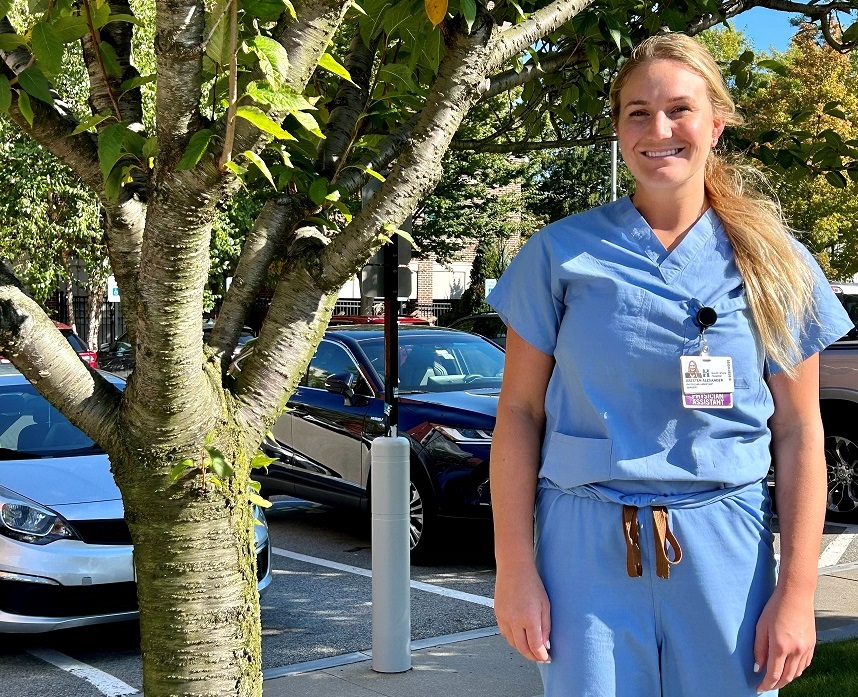 A female physician assistant poses next to a tree outside the hospital