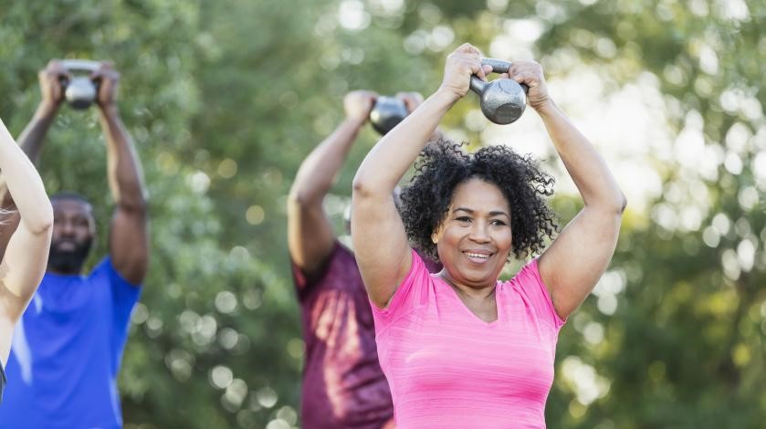 A Black woman works out with weights in a group outdoors