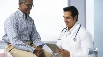Middle aged Black patient sitting on exam table talking to his doctor