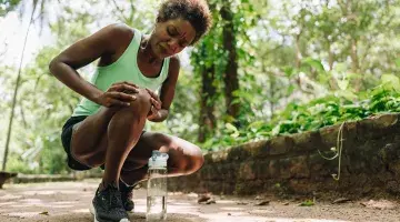 A black woman out for a run bends down to rub her arthritic knee
