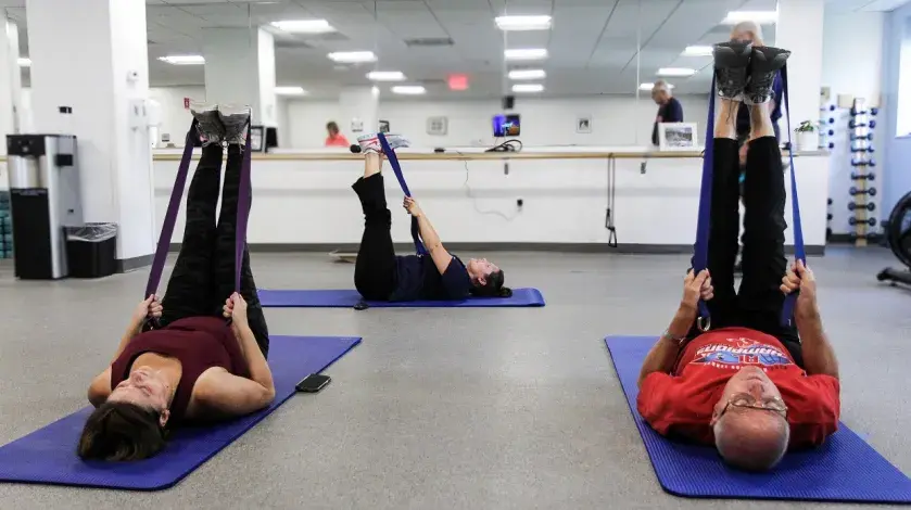 Three people on their backs on exercise mats in a class