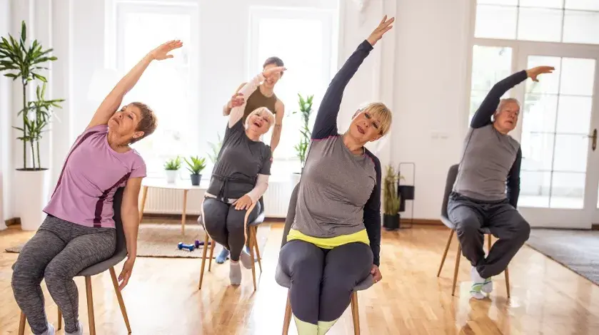 An instructor leads four older adults in a chair yoga class