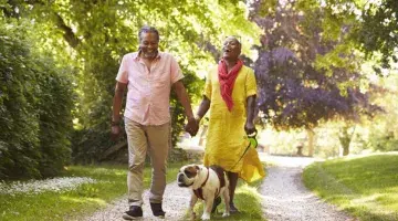 An older Black couple outside walking their bulldog