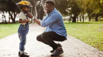 A dad adjusts the strap on his son's bike helmet