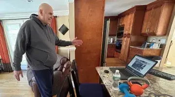 A man exercising in his kitchen to a virtual fitness class on a laptop