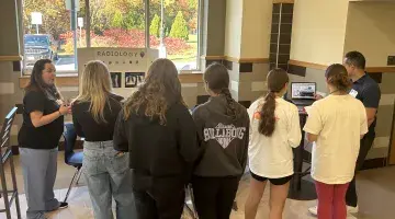 Students stand in front of display boards as two South Shore Health colleagues share info on healthcare careers at a high school career event.