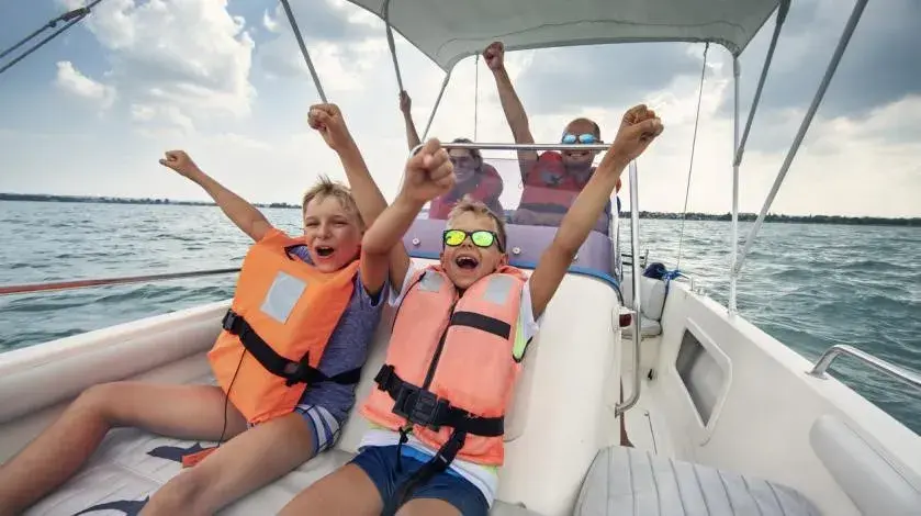 Two young boys in life jackets cheering on a boat