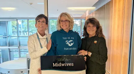 Three midwives from South Shore Health pose for a photo holding a sign promoting meet the midwives sessions