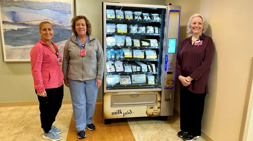 Three colleagues from South Shore Hospital stand next to a MilkPod vending machine.